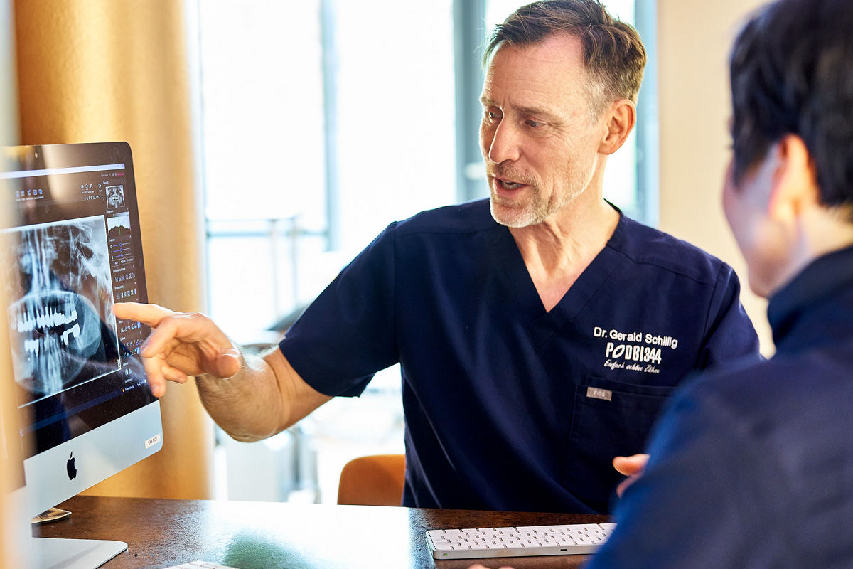 Zahnarzt Dr. Schillig von der Zahnarztpraxis Podbi344 in Hannover erklärt einem Patienten ein digitales Röntgenbild.