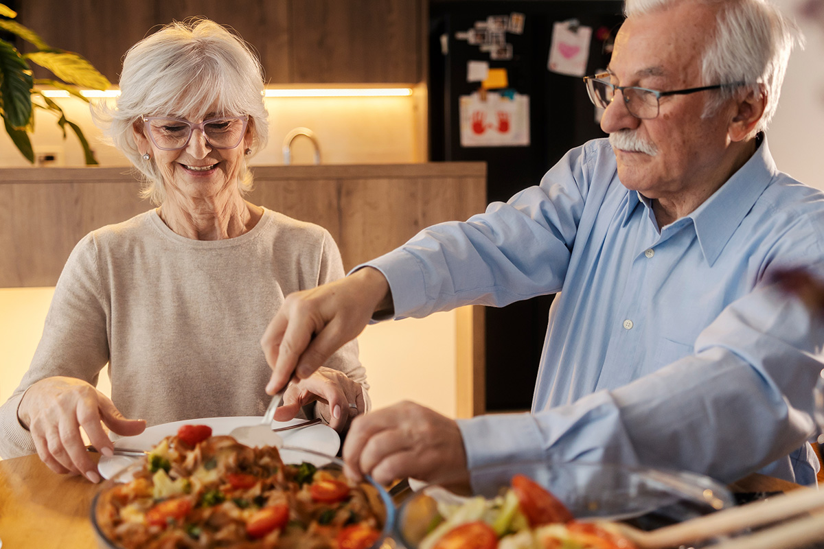 Älteres Paar genießt Mahlzeit. Gesunde Ernährung ist wichtig für die Mundgesundheit, beraten wir Sie in der Zahnarztpraxis Podbi344 Hannover.