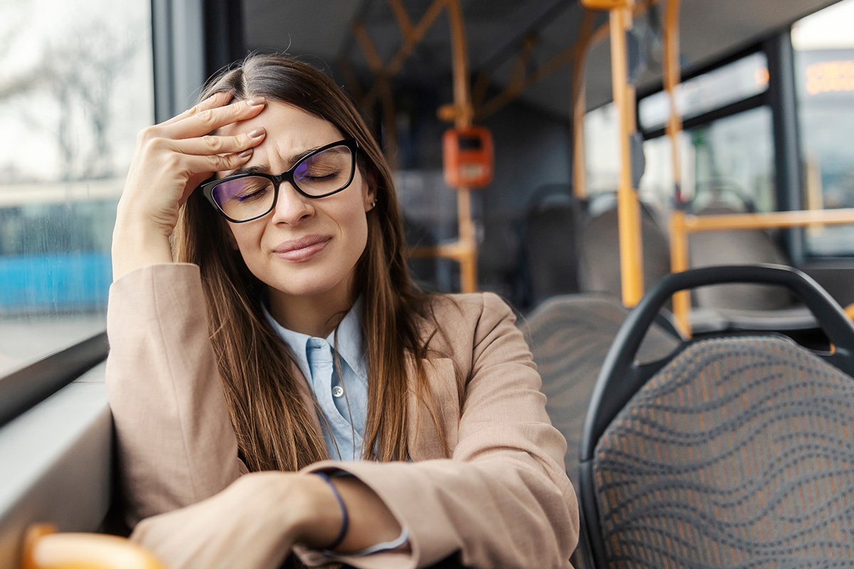 Frau mit Kopfschmerzen im Bus benötigt möglicherweise eine Zahnbehandlung in der Zahnarztpraxis Hannover.